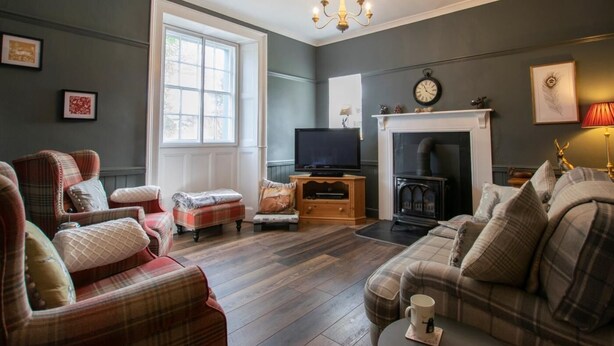 A cozy living room with a fireplace, television, and plaid furniture. - 3 Bed in Penrith (oc-74159) (Shap)
