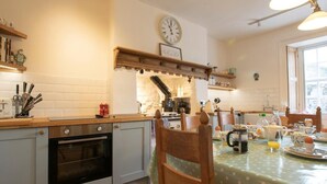 A kitchen with a wooden countertop, an oven, a dining table with a polka dot tablecloth, and a clock on the wall. - 3 Bed in Penrith (oc-74159) (Shap)