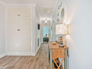 A hallway with a wooden floor, a white door with star decorations, a wall-mounted mirror, and a table with a lamp and decorative items.
