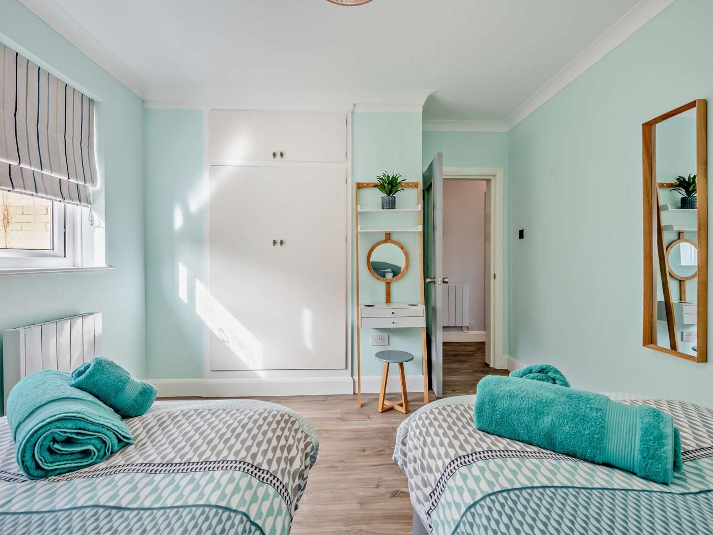 Een slaapkamer met twee bedden, een kledingkast, een spiegel en een kleine plant.