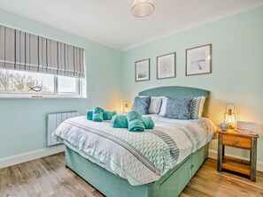 A bedroom with a bed, bedside table, lamp, and framed pictures on the wall.