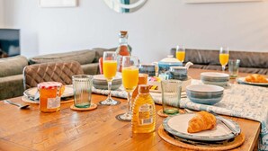 Une table dressée pour le petit-déjeuner, avec des aliments typiques du petit-déjeuner, et un canapé en arrière-plan.