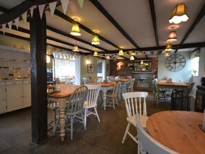 Interior de restaurant amb taules i cadires de fusta, lluminàries penjants i una paret de maó.