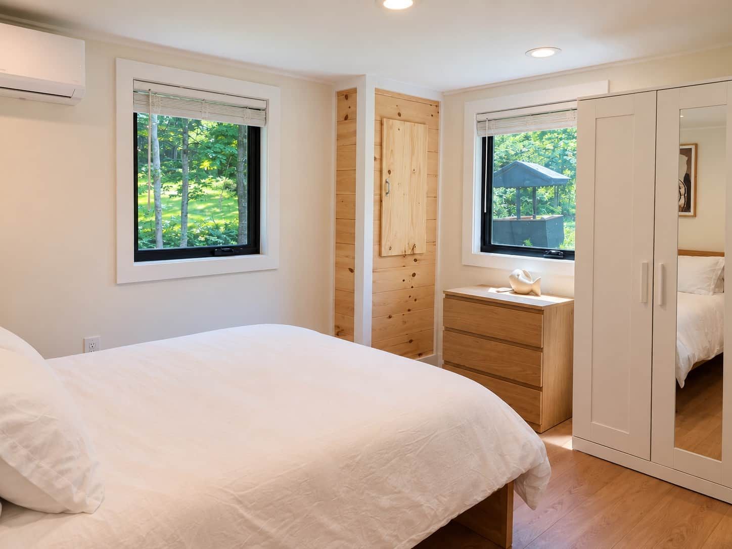 Un dormitorio con cama, armario de madera, cómoda pequeña y ventana con vista a la vegetación.