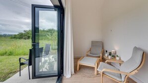 Un balcón con puerta de vidrio, una silla, una mesa y vista a un campo cubierto de hierba.
