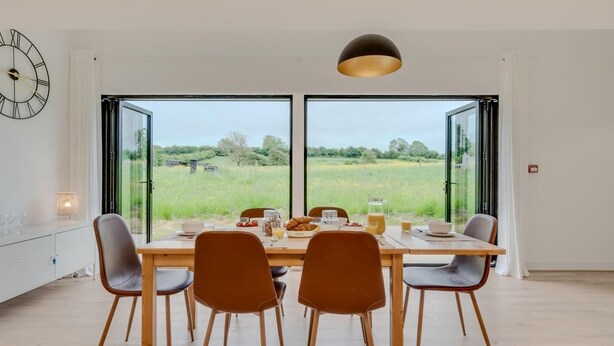 Comedor con mesa preparada para cuatro personas, ventanas amplias y una lámpara colgante moderna.