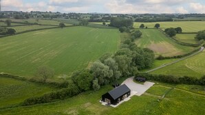 Vista aérea de un paisaje rural con una casa negra solitaria rodeada de campos verdes y árboles.