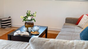 Un salón con un sofá, una mesa de centro con un libro, tetera, tazas y galletas.