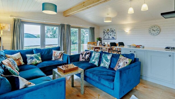 A cozy living room with blue sofas, a coffee table, and a dining area with a kitchen in the background. - 4 Bed in Shrewsbury (oc-93398) (Sheinton)