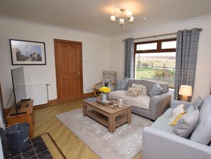A living room with a sofa, a coffee table, a lamp, a radiator, a door, and a window with curtains.