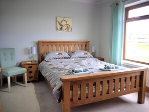 A bedroom with a wooden bed, a bedside table with a lamp, a chair, and a window with curtains. - 3 Bed in Isle Of Skye (oc-88639) (Ose)