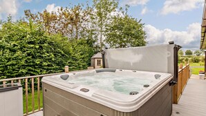 Een hottub op een houten terras met uitzicht op bomen en een huis op de achtergrond.