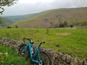 A bicycle leaning against a stone wall in a grassy field with a hill in the background. - 3 Bed in Buxton (oc-94110) (Cressbrook)