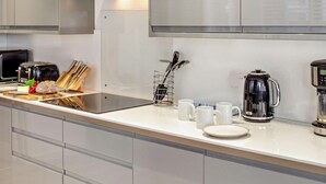 Et moderne køkken med emhætte i rustfrit stål, en brødrister, et knivblok, en kaffemaskine og en elkedel på disken.