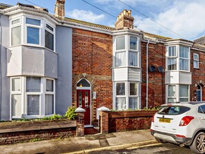 A corner house with a bay window, a red door, and a white car parked in front. - 4 Bed in Weymouth (oc-86369) (Weymouth)