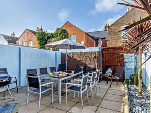 An outdoor patio with a table and chairs, a grill, and a blue wall. - 4 Bed in Weymouth (oc-86369) (Weymouth)