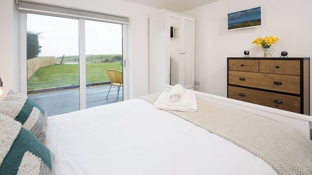 A bedroom with a bed, a dresser, a chair, and a view of a grassy area through a sliding door. - 3 Bed in Belford (oc-cn065) (Easington)