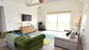 A living room with a green sofa, a grey sofa, a wooden cabinet, a fireplace, and a large sliding glass door. - 3 Bed in Belford (oc-cn065) (Easington)