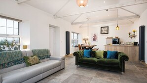 A spacious living area with a sofa, a green velvet sofa, a dining table, and a kitchen area with a microwave and a sink. - 3 Bed in Belford (oc-cn065) (Easington)