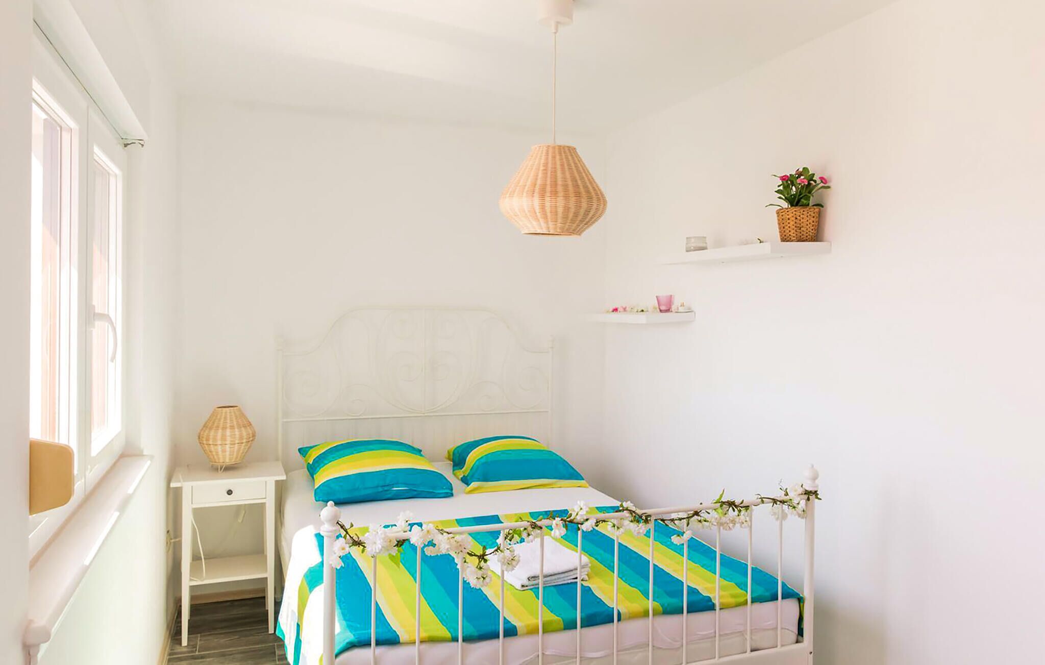 Ein Schlafzimmer mit Bett, Nachttisch, Deckenleuchte und Fenster.