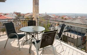 Ein Balkon mit rundem Tisch und vier Stühlen, der auf eine Stadt mit roten Dächern blickt.