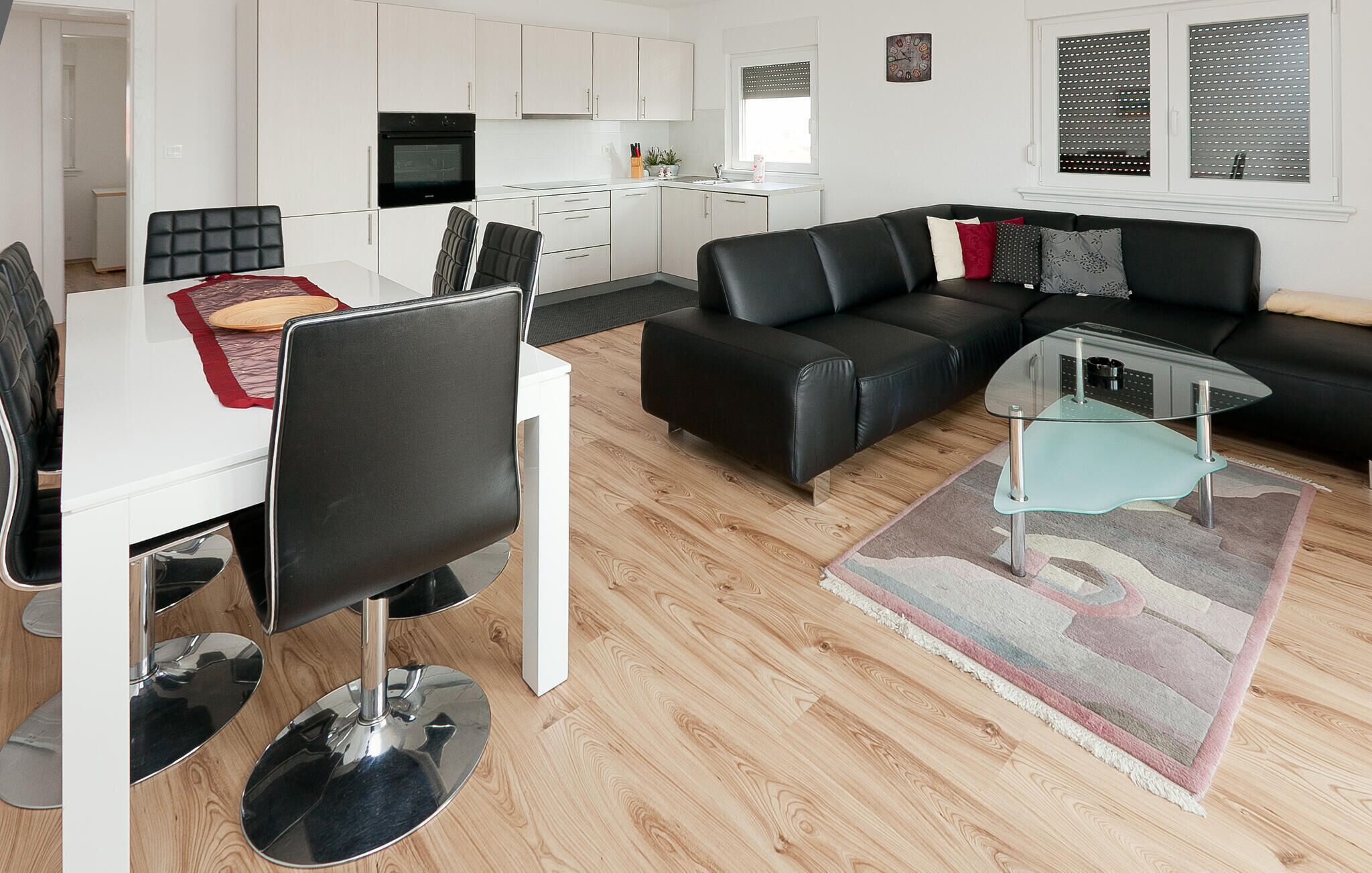 Ein modernes Wohnzimmer mit Essbereich, einer schwarzen Ledersofa, einem Glastisch und einer Küche im Hintergrund.
