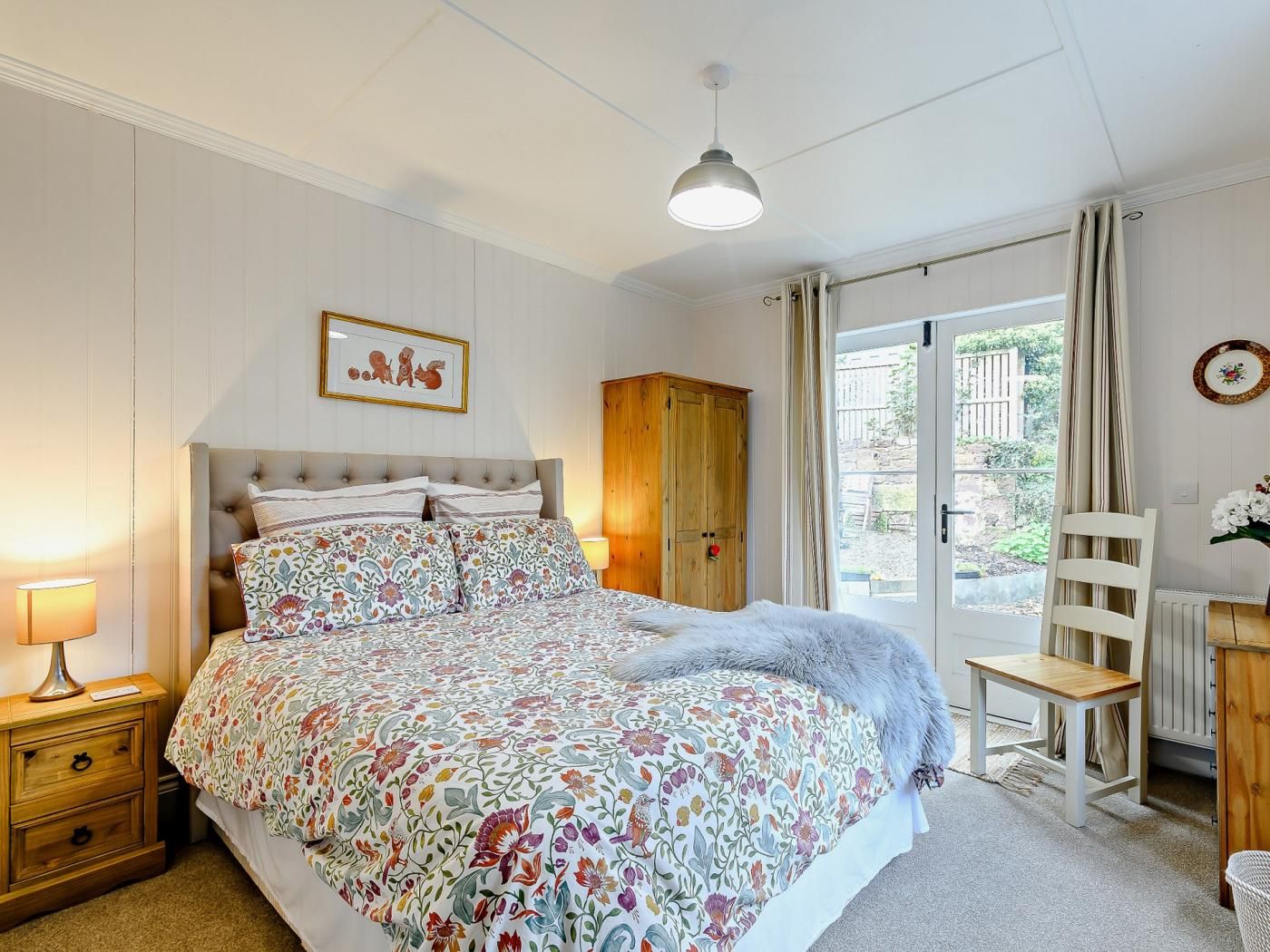 Ein Schlafzimmer mit einem Bett, einem Nachttisch, einem Holzschrank, einem Stuhl, einem Tisch und einem Fenster mit Vorhängen.