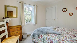 Ein Schlafzimmer mit Bett, Kommode, Spiegel, Fenster mit Vorhängen und einer Tür.