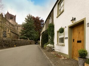 Eine schmale Gasse mit einem Steinhäuschen links und einem weißen Gebäude mit Holztür rechts.