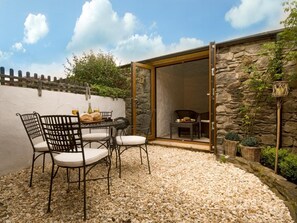 Eine Terrasse im Freien mit Tisch und Stühlen, einer Steinmauer und Blick ins Innere.