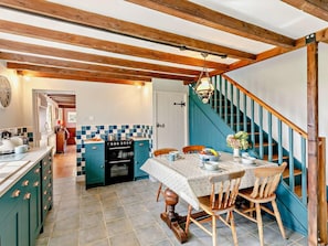 Eine Küche mit Holzbalkendecke, einer blauen Treppe und einem Essbereich mit Tisch für vier Personen.