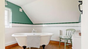 A bathroom with a freestanding bathtub, a radiator, a chair, and a window. - 3 Bed in Market Rasen (oc-93253) (Ranby)