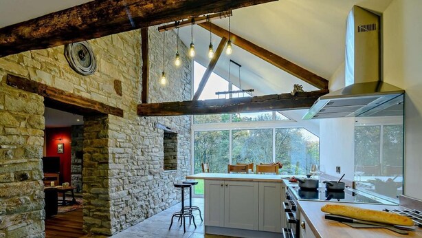 A kitchen with stone walls, wooden beams, a large window, and a modern stove. - 3 Bed in Brecon (oc-93680) (Llandefalle)