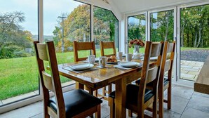 A dining area with a table set for four, large windows, and a view of a grassy landscape. - 3 Bed in Brecon (oc-93680) (Llandefalle)