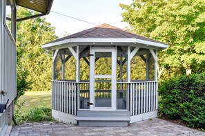 A gazebo with a white exterior and a dark roof, surrounded by greenery. - Relaxing Waterfront Cottage (Prince Edward)
