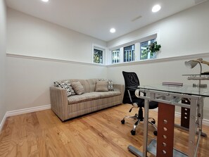 A room with a sofa, a desk with a chair, and a window with a plant. - Relaxing Waterfront Cottage (Prince Edward)