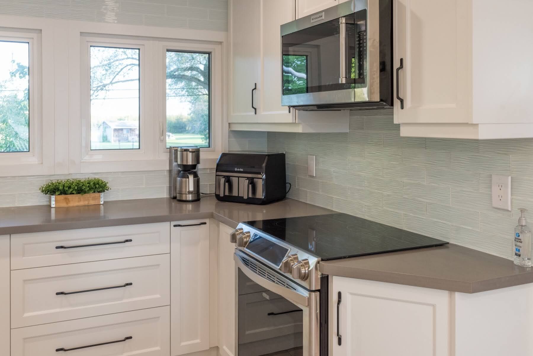 A modern kitchen with white cabinetry, a built-in microwave, a coffee maker, and a stove.