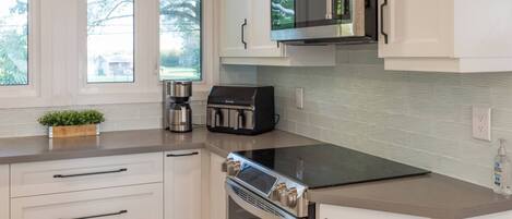 A modern kitchen with white cabinetry, a built-in microwave, a coffee maker, and a stove.