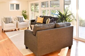 A living room with a grey sofa, two armchairs, a coffee table, and a large window with a view of greenery. - Relaxing Waterfront Cottage (Prince Edward)