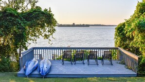 Een houten terras met stoelen en kajaks, met uitzicht op een kalm wateroppervlak.