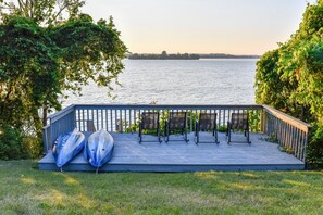 Eine Holzterrasse mit Stühlen und Kajaks, mit Blick auf ruhiges Gewässer.