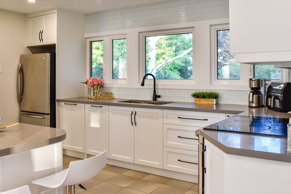 A modern kitchen with white cabinets, a stainless steel refrigerator, a sink with a black faucet, and a coffee maker.