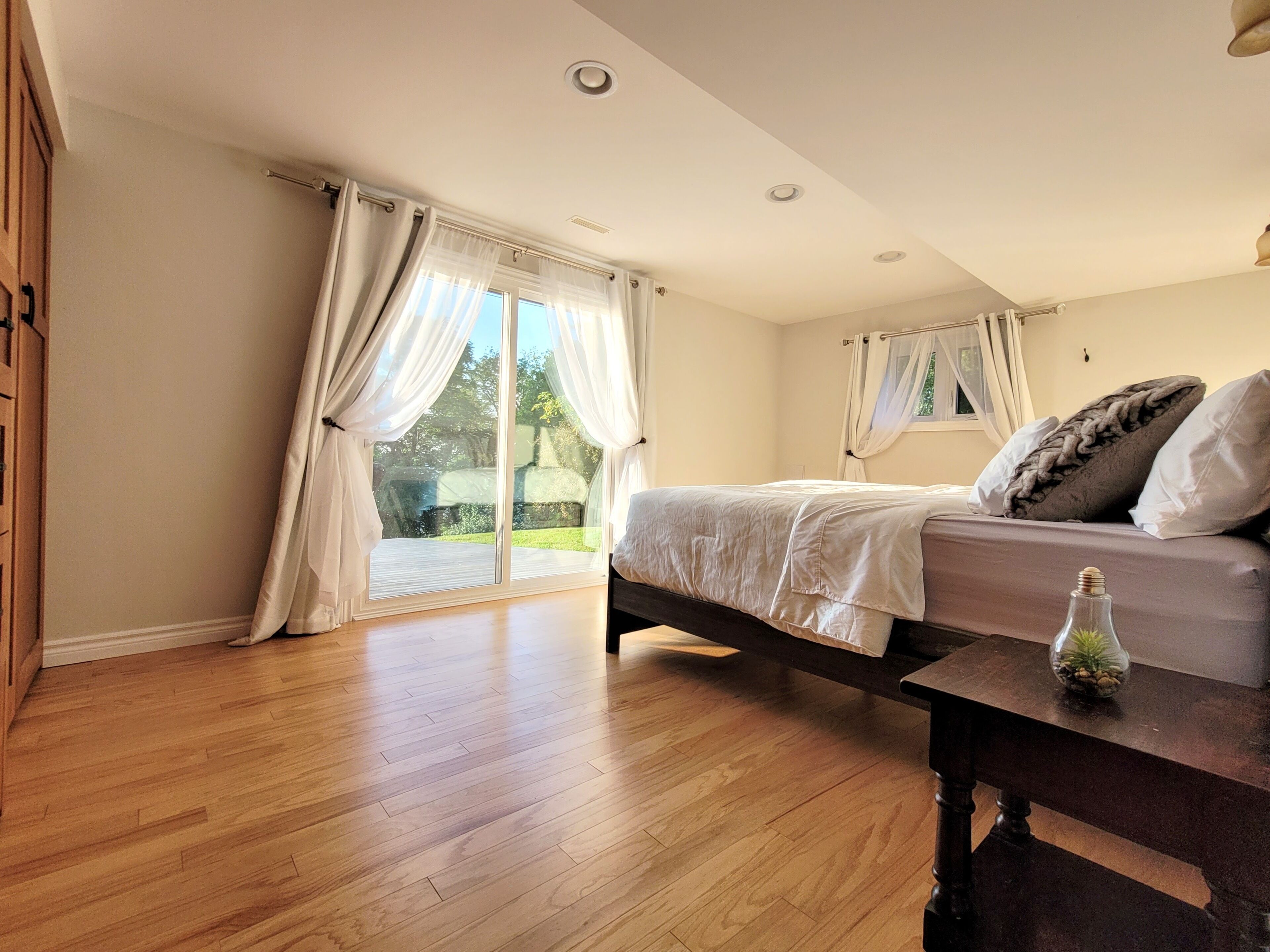 A bedroom with a bed, wooden floor, and a window with curtains.