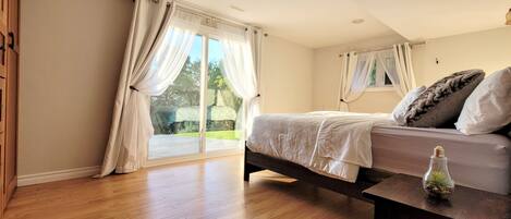 A bedroom with a bed, wooden floor, and a window with curtains.