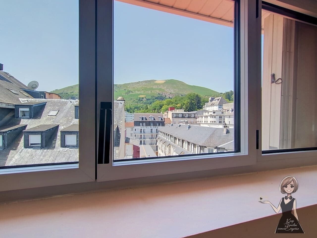 A view through a window of a building with multiple floors, a visible hotel named 'HOTEL GLORIA,' and a green hill in the background.