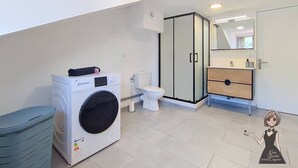 Et moderne badeværelse med vaskemaskine, toilet og brusekabine i glas.