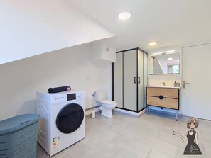 Ein modernes Badezimmer mit Waschmaschine, Toilette und einer Duschkabine aus Glas.
