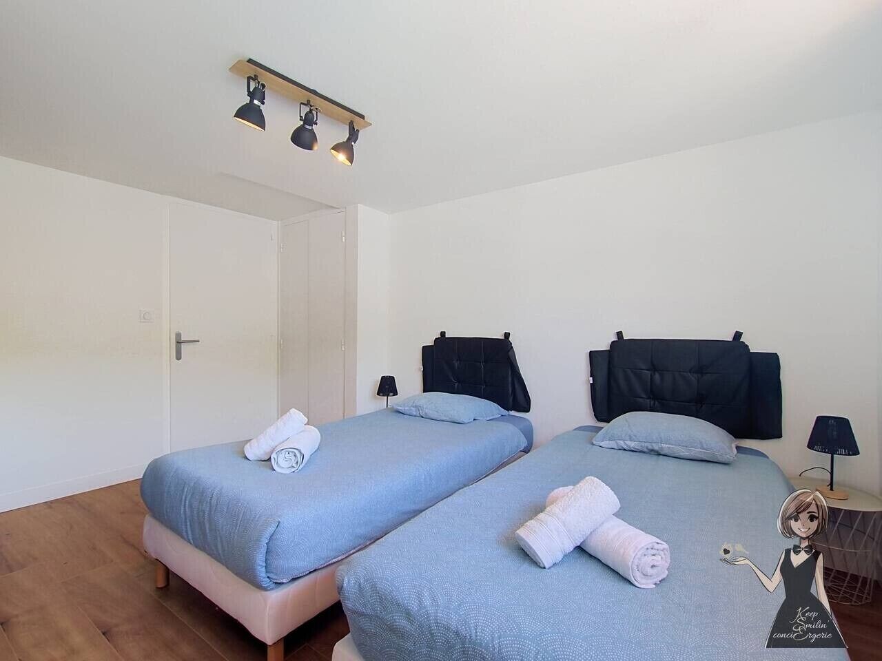 Ein Zimmer mit zwei Betten, einer Tür, einer Lampe und einem an der Wand befestigten Regal.