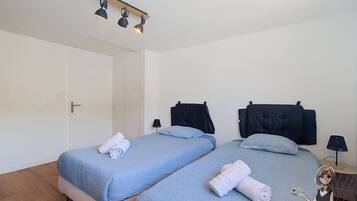 Ein Zimmer mit zwei Betten, einer Tür, einer Lampe und einem an der Wand befestigten Regal.