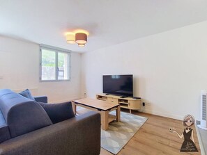 Un salon moderne avec un canapé, une table basse, un téléviseur et une petite table avec une lampe.